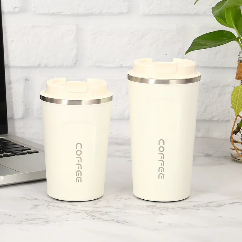 Two cream-colored insulated coffee cups with 'COFFEE' text on a marble surface next to a laptop.