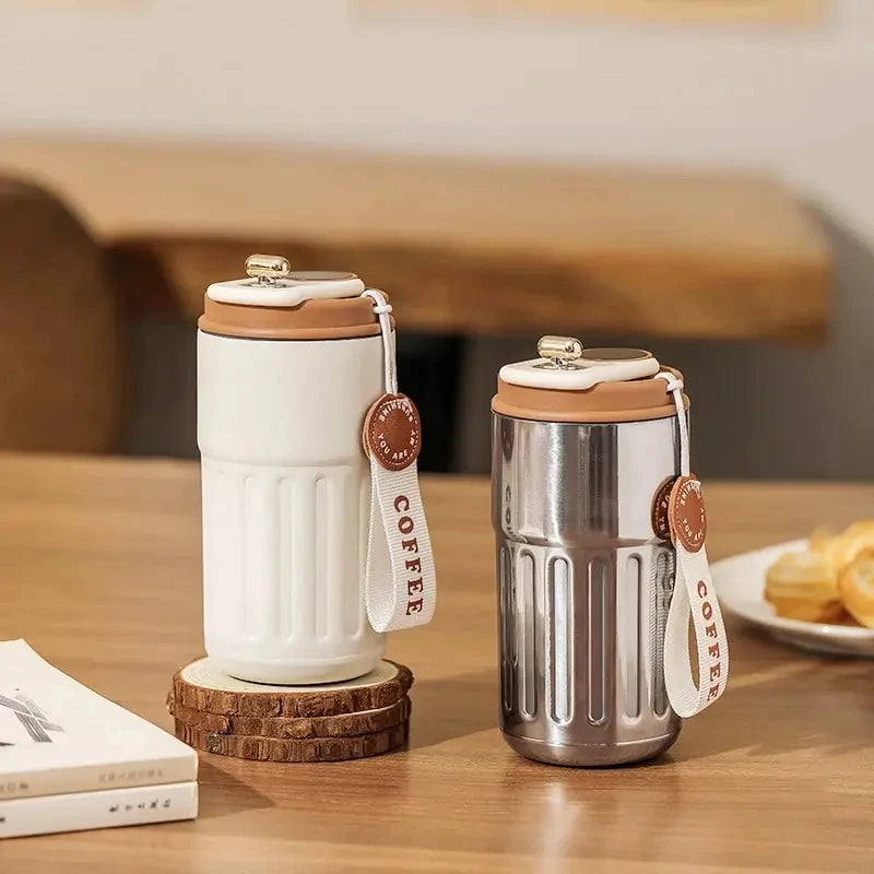 Two coffee thermos bottles on a wooden surface with a blurred background