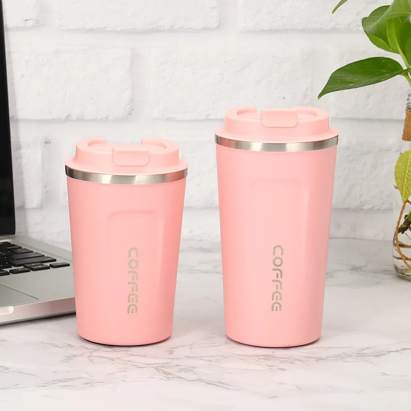 Two pink insulated coffee tumblers with silver lids on a desk next to a laptop.