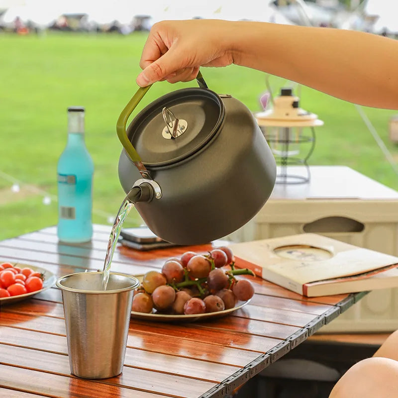 Person pouring liquid from a kettle into a cup on a wooden table outdoors.