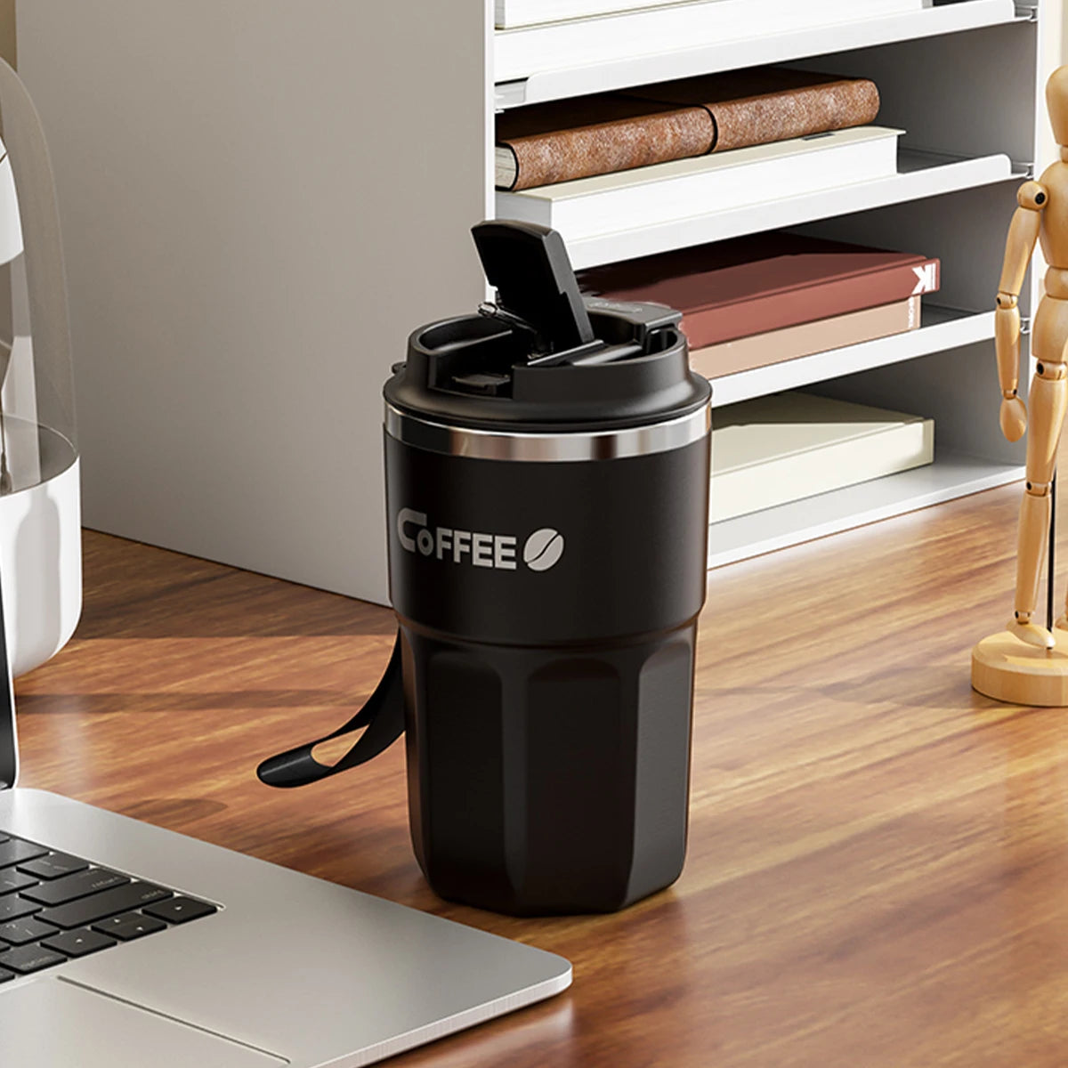 Black coffee tumbler with 'COFFEE' text on a wooden desk next to a laptop.