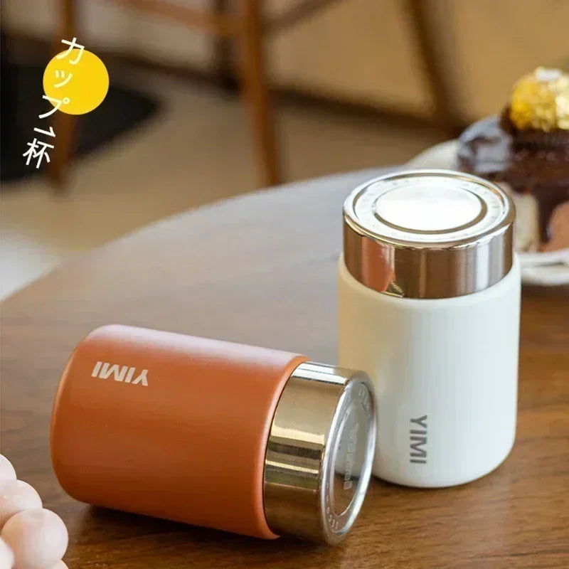 Two YIMI thermos cups, one orange and one white, on a wooden table.