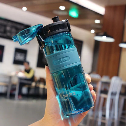 Blue water bottle with black cap held in a hand, blurred indoor background