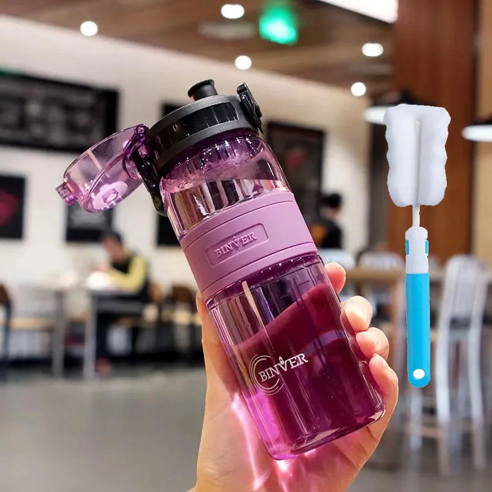 Pink water bottle with black lid held in a hand, with a blurred indoor background