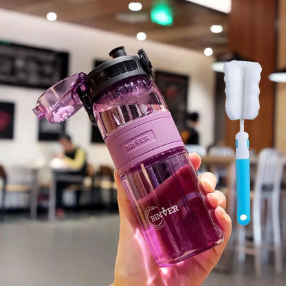 Pink water bottle with black lid held in a hand, with a blurred indoor background