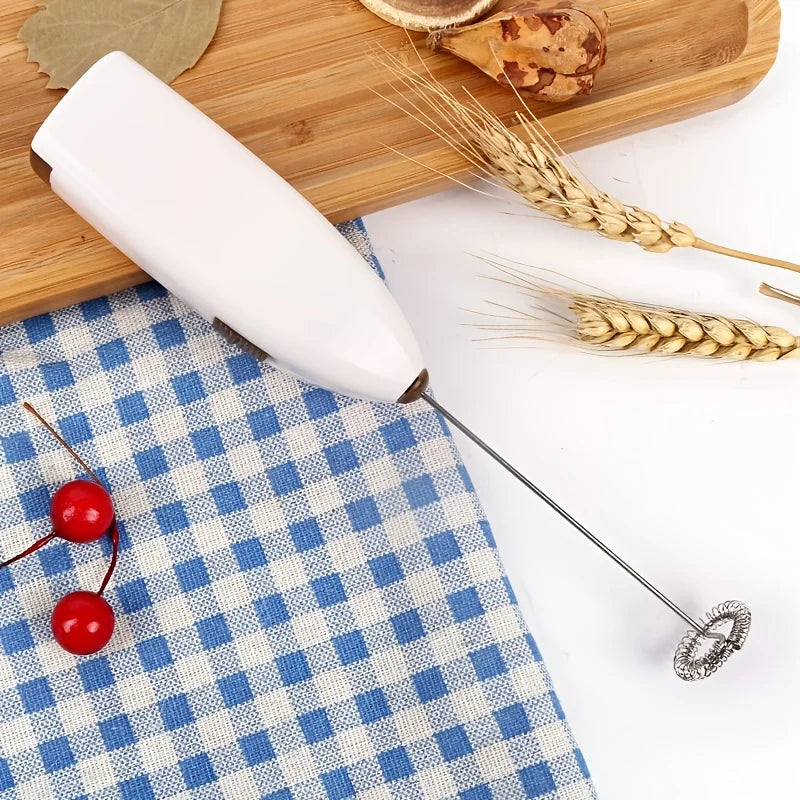 White whisk on a blue and white checkered tablecloth with wheat stalks and red cherries.