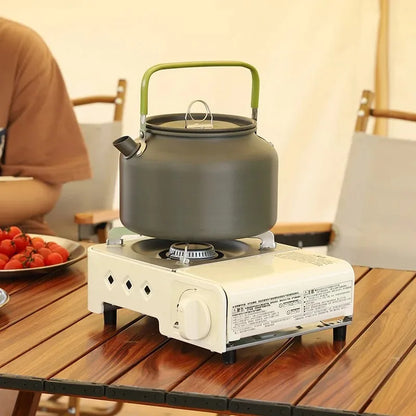 Portable stove with a kettle on a wooden table, with a blurred background of people and food.
